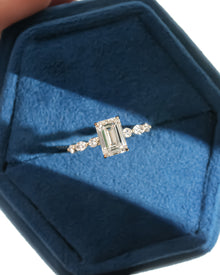 Top view of an emerald cut lab grown diamond ring with marquise and round side diamonds in a blue velvet ring box