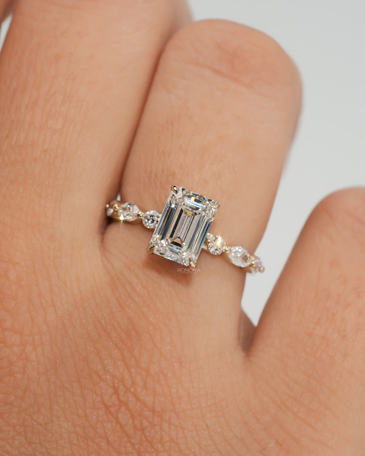Emerald cut lab grown diamond ring in yellow gold with alternating round and marquise side diamonds, worn on a finger