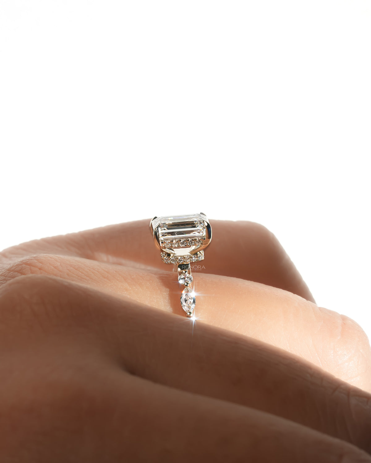 Side profile close-up of an emerald cut lab grown diamond ring on a hand, showing the diamond halo and marquise side stone