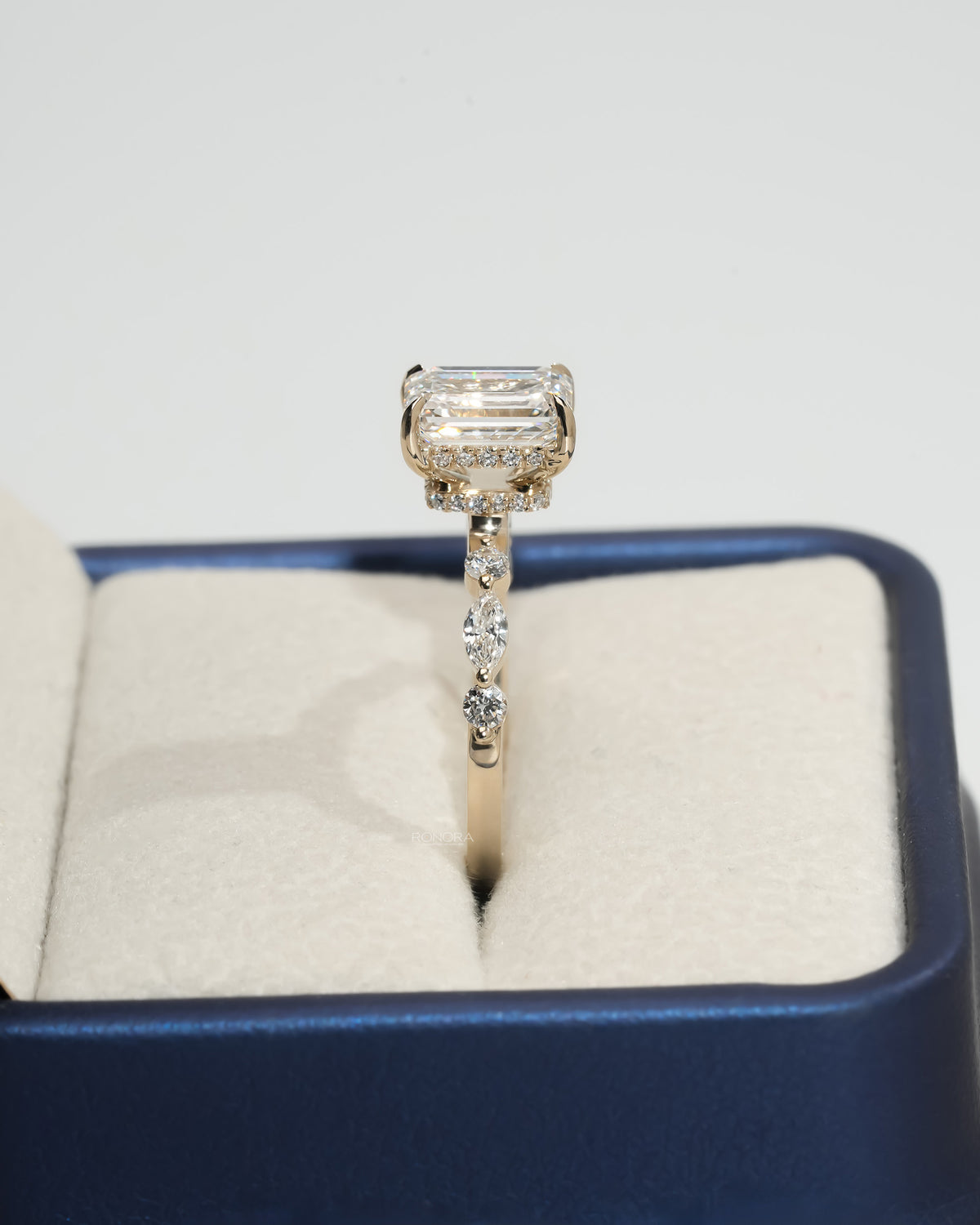 Side view of an emerald cut lab grown diamond ring in a jewelry box, showing the yellow gold band and diamond halo