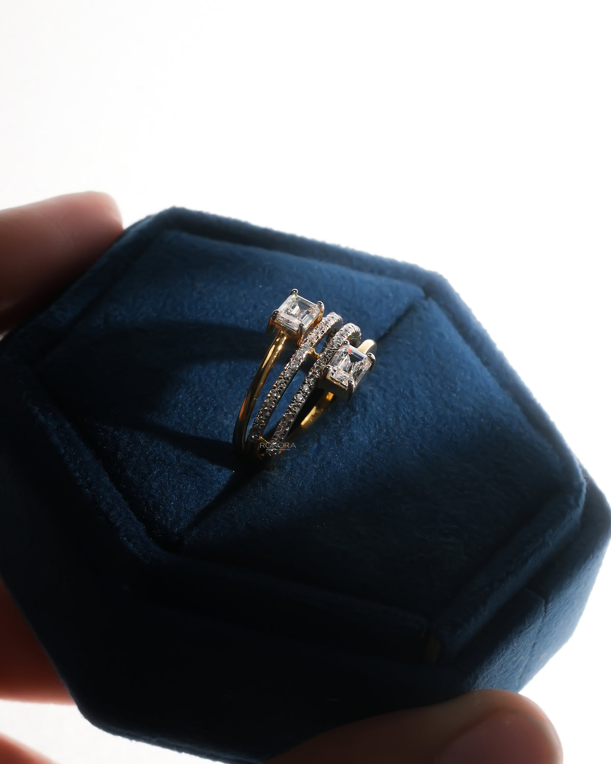 Angled view of a toi et moi lab grown diamond ring with two emerald cut stones resting in a blue velvet ring box