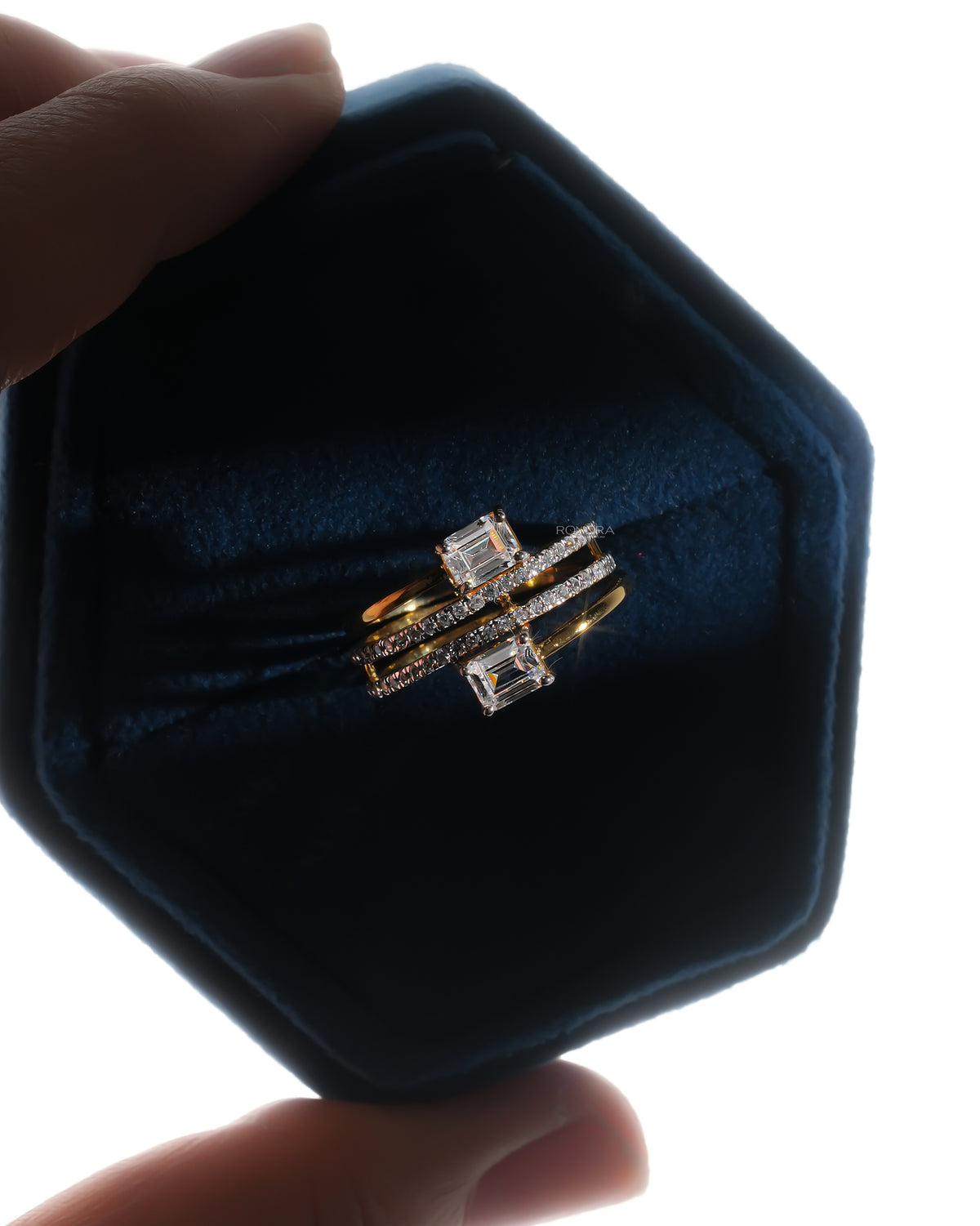 Emerald cut toi et moi lab grown diamond ring in a blue velvet hexagon ring box, yellow gold wrap band, top view