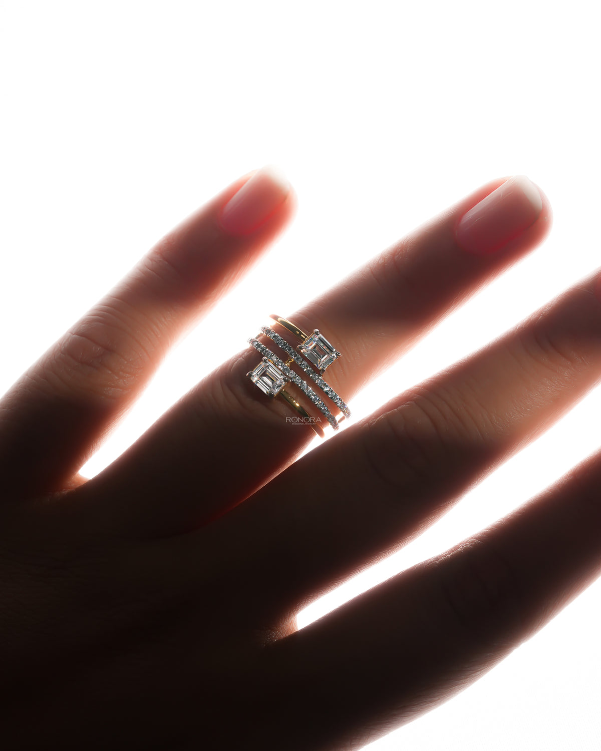 Toi et moi lab grown diamond ring with two emerald cut stones and pave wrap bands, worn on a backlit hand