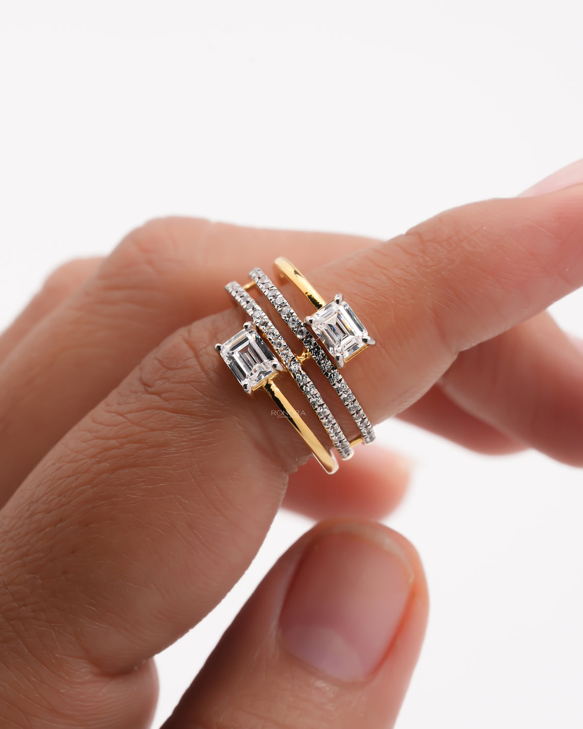 Close-up of a toi et moi lab grown diamond ring on a finger, two emerald cut stones with pave diamond wrap bands
