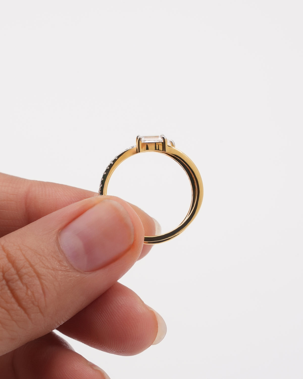 Side view of a yellow gold wrap band lab grown diamond ring held between two fingers, emerald cut stone on top