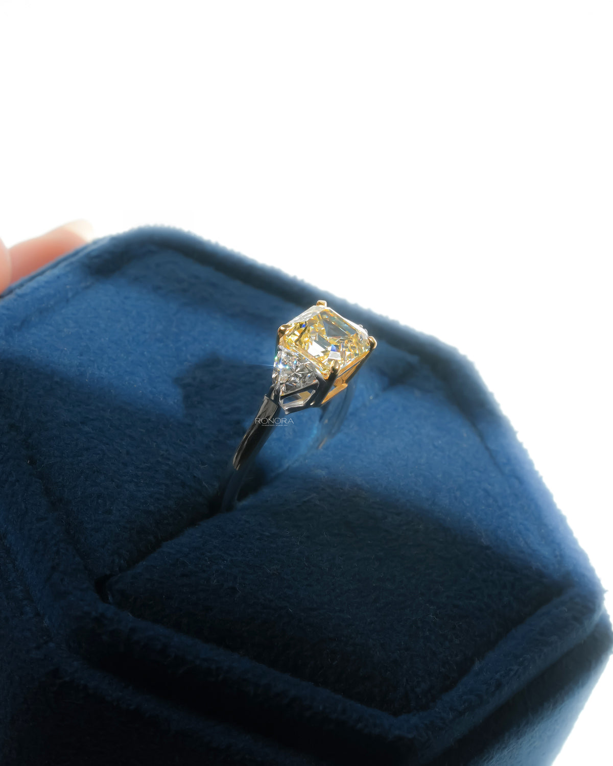 Angled side view of a fancy yellow lab grown diamond ring in a blue velvet ring box with white side stones