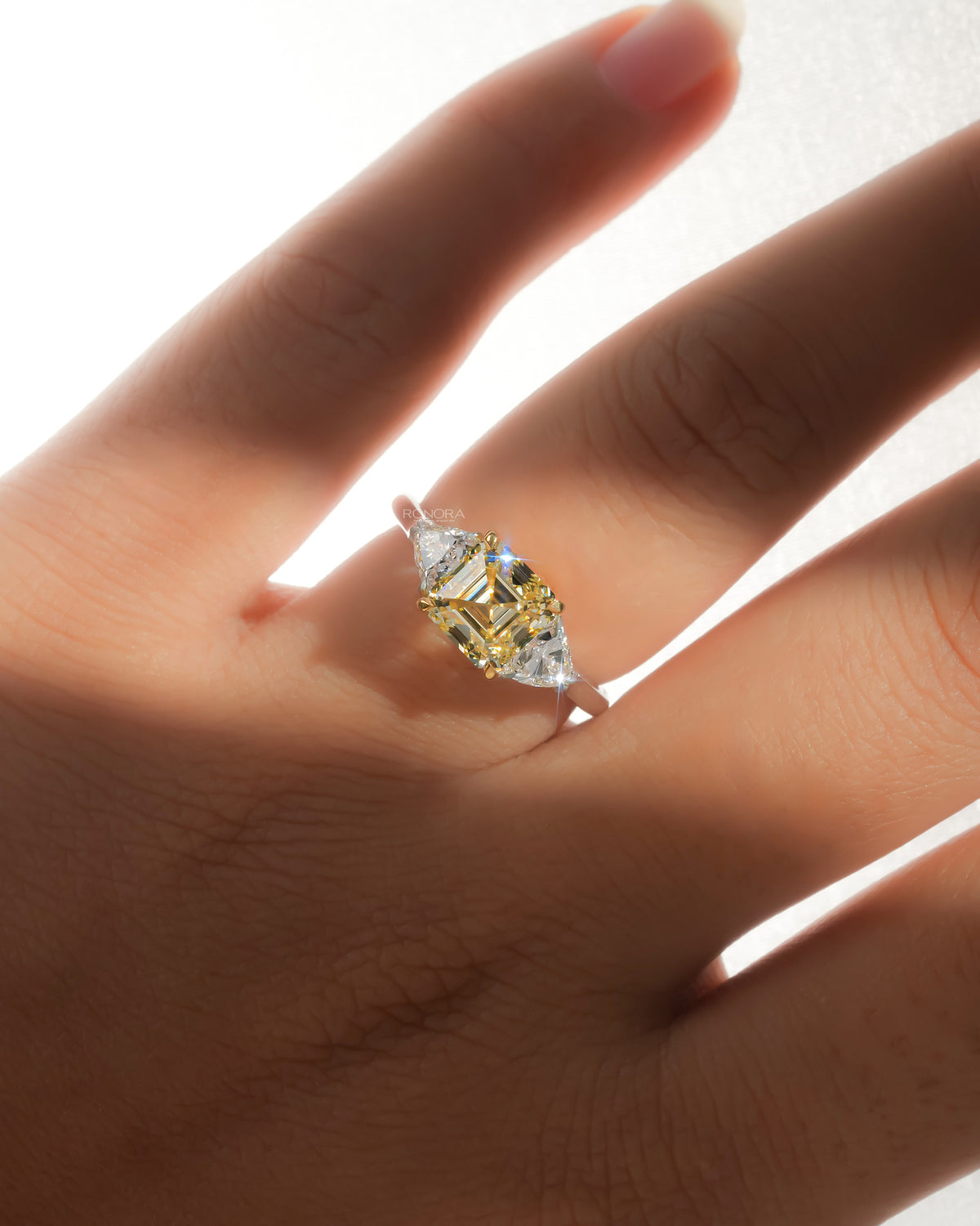 Fancy yellow lab grown diamond ring with side stones worn on a hand, backlit with sunlight sparkle