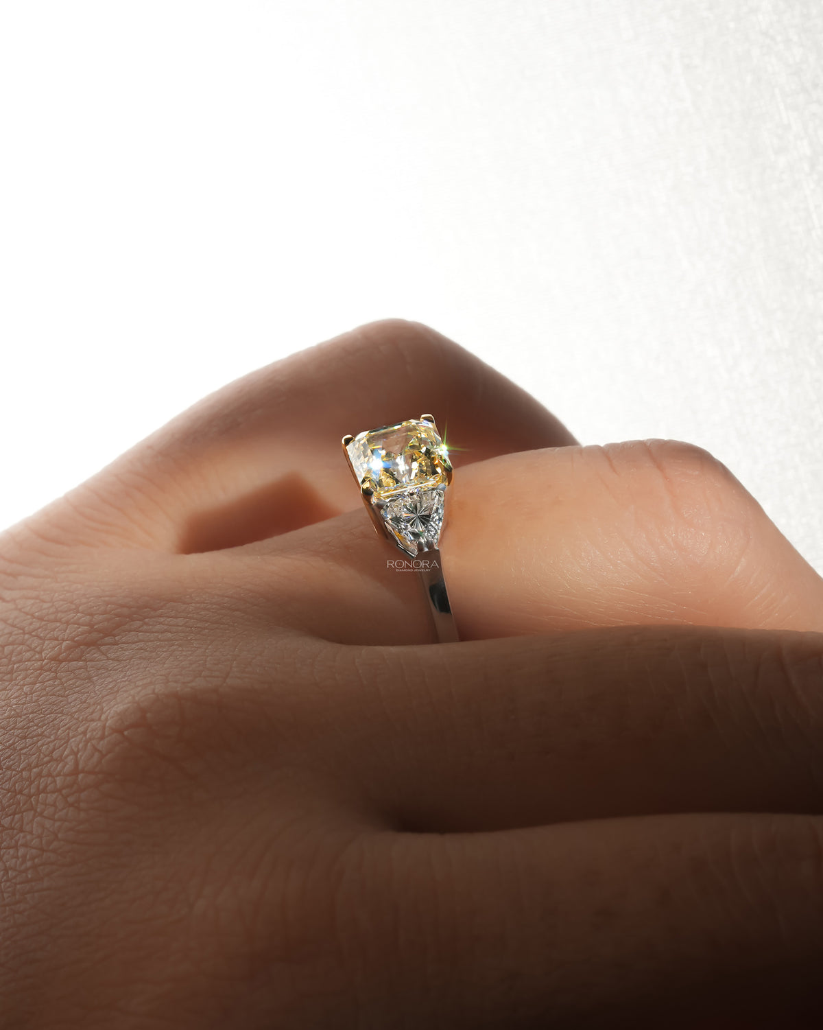 Side view of a fancy yellow lab grown diamond ring with white side stones worn on a finger, close-up