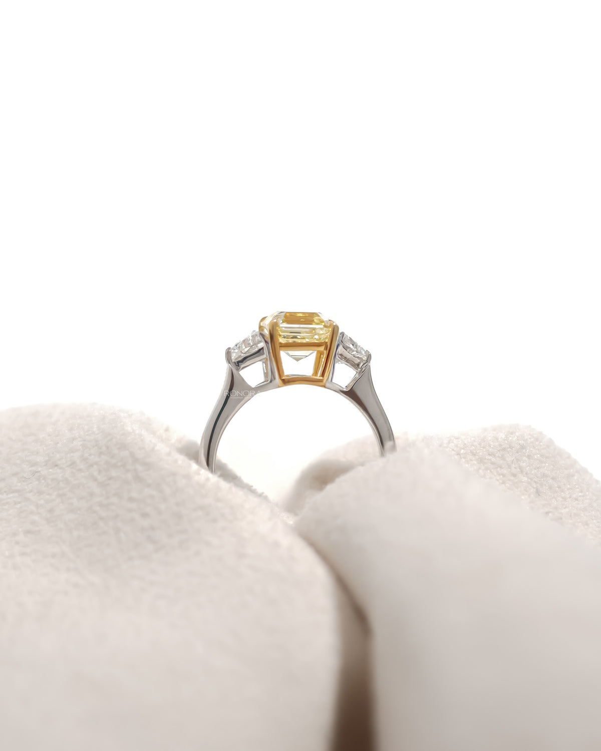 Back view of a fancy yellow lab grown diamond ring with white side stones and gold prongs on cream velvet