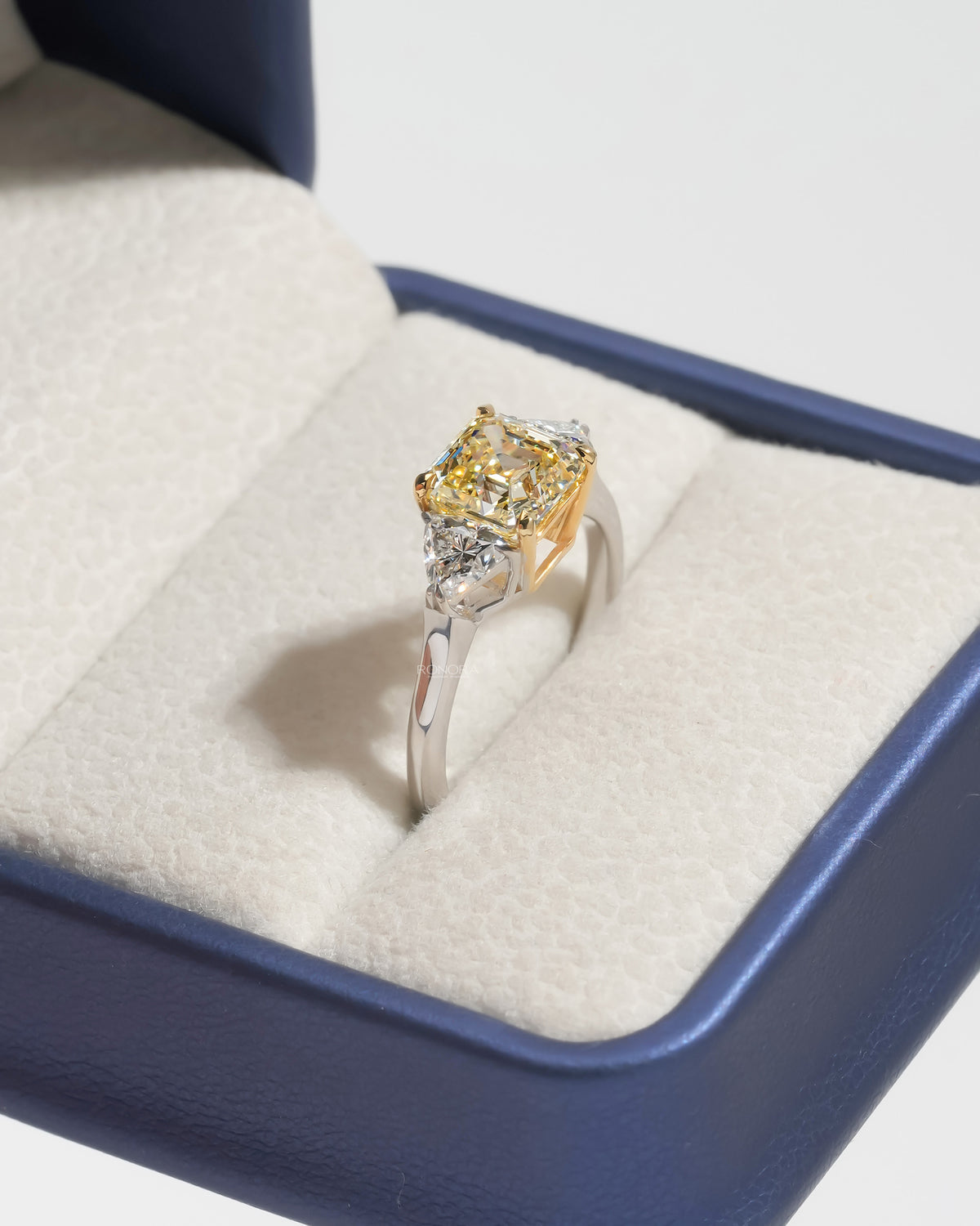 Fancy yellow lab grown diamond ring with white side stones, angled in a cream and blue ring box