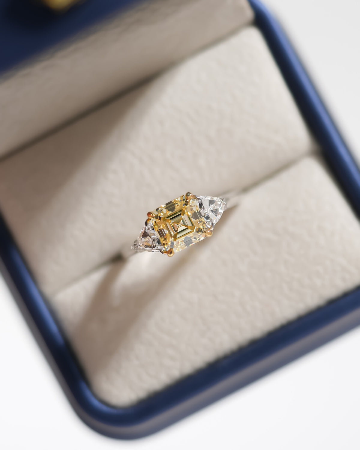 Fancy yellow lab grown diamond ring with white side stones, top view in a cream ring box with blue rim