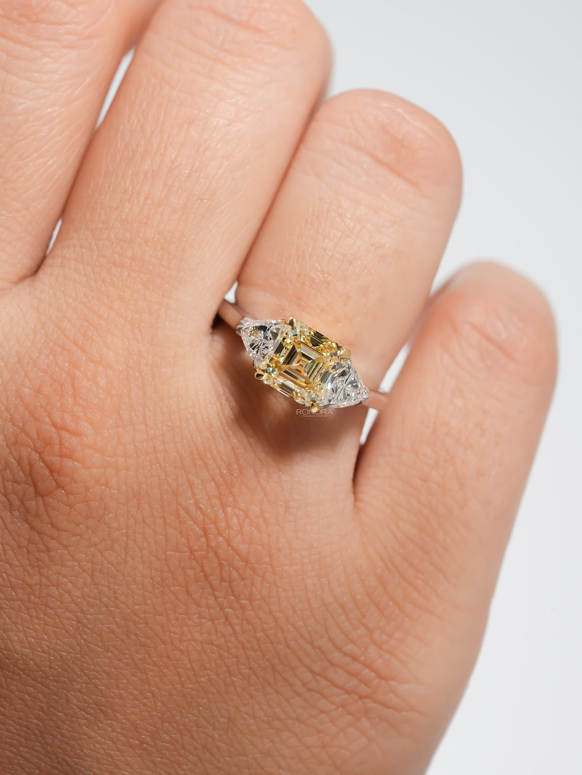 Fancy yellow lab grown diamond ring with two white side stones worn on a hand, front view close-up