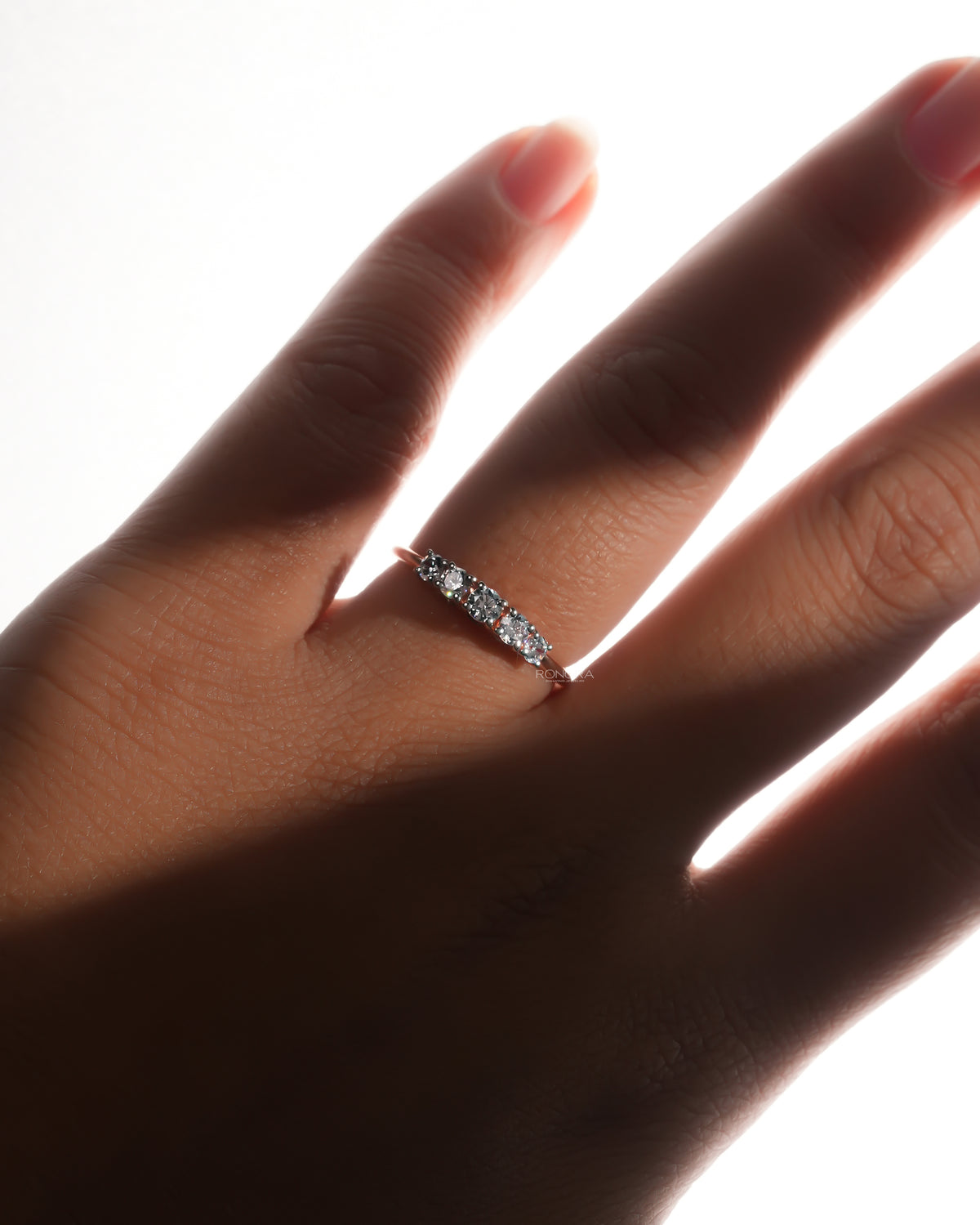 Five stone lab grown diamond pinky ring with graduated round stones, worn on a hand in soft backlight