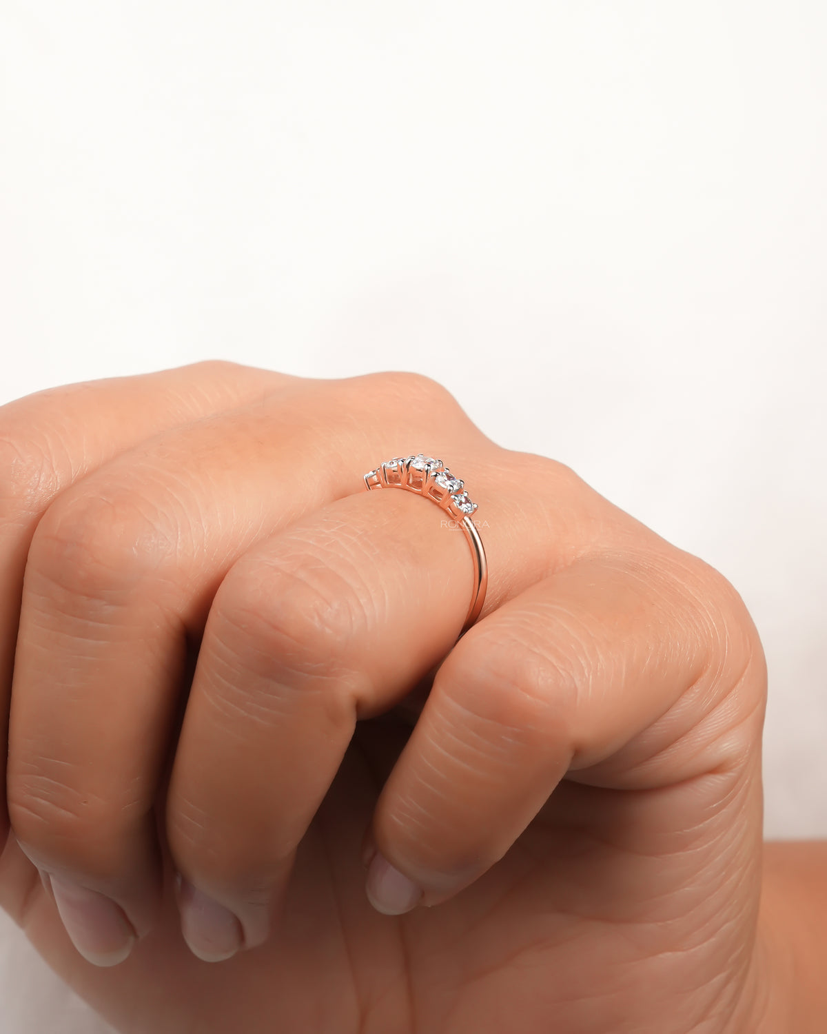 Angled view of a rose gold five stone lab grown diamond pinky ring worn on a finger with graduated round stones