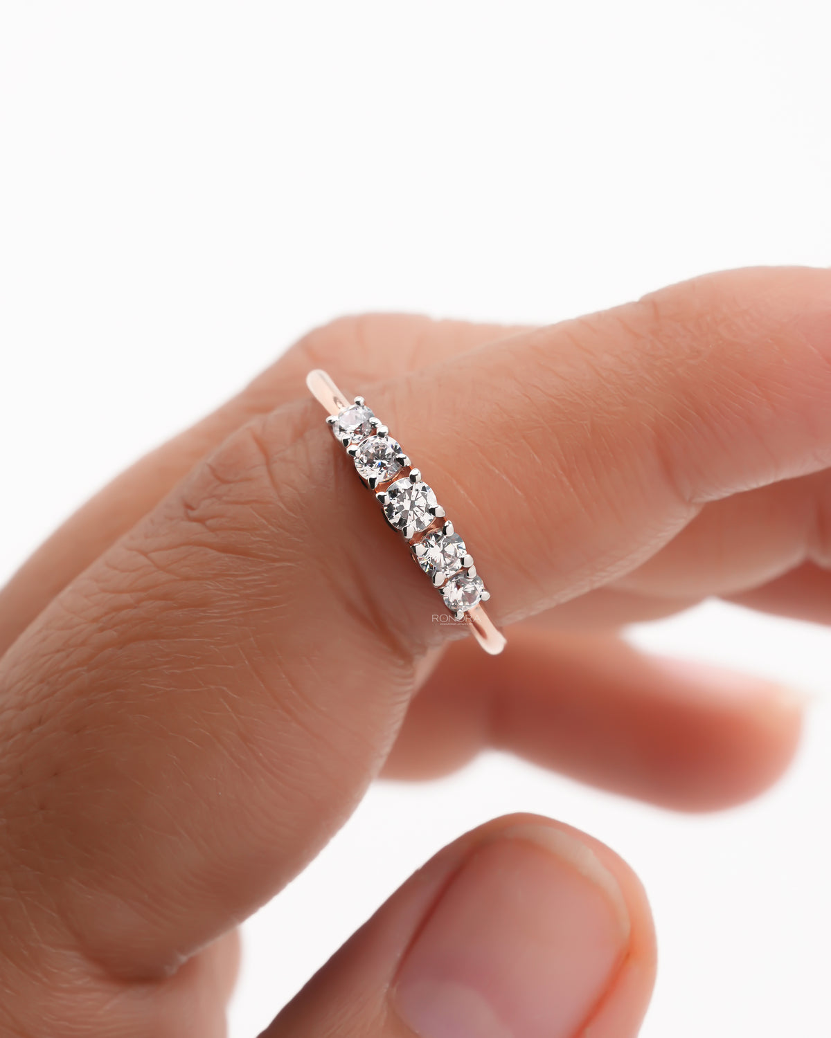 Close-up of a rose gold five stone lab grown diamond pinky ring on a fingertip showing the prong set round stones