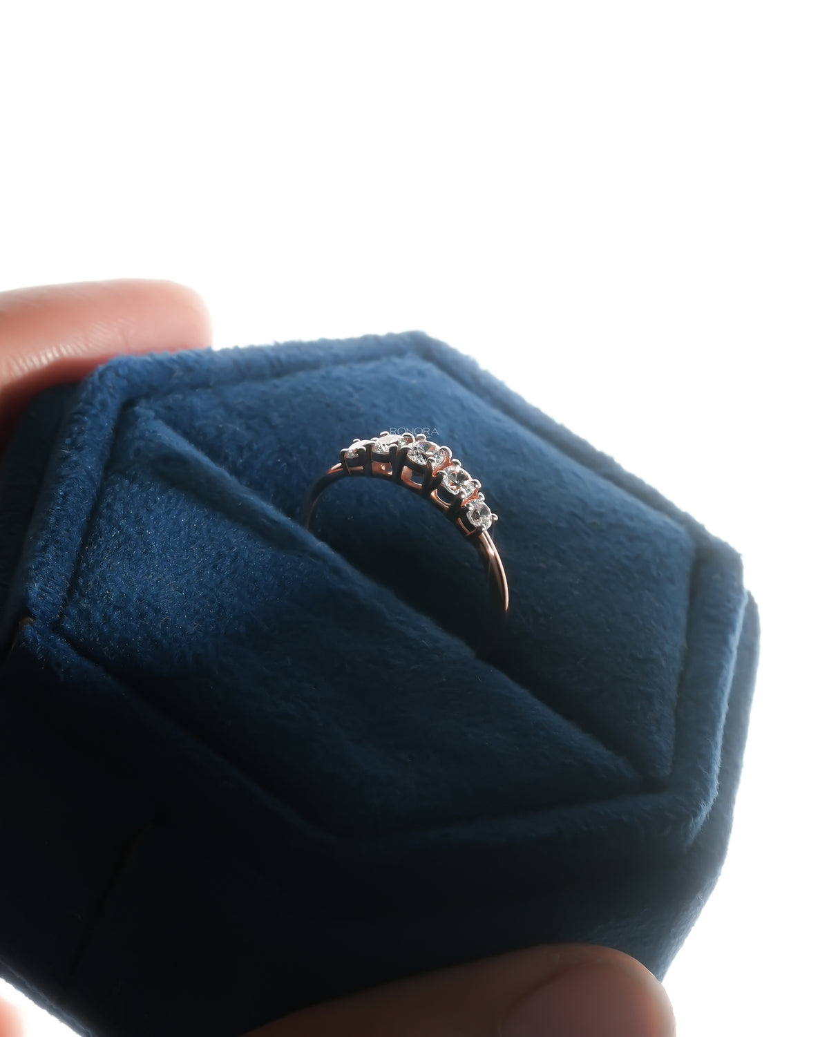 Five stone lab grown diamond pinky ring in rose gold standing in a navy velvet ring box held in hand