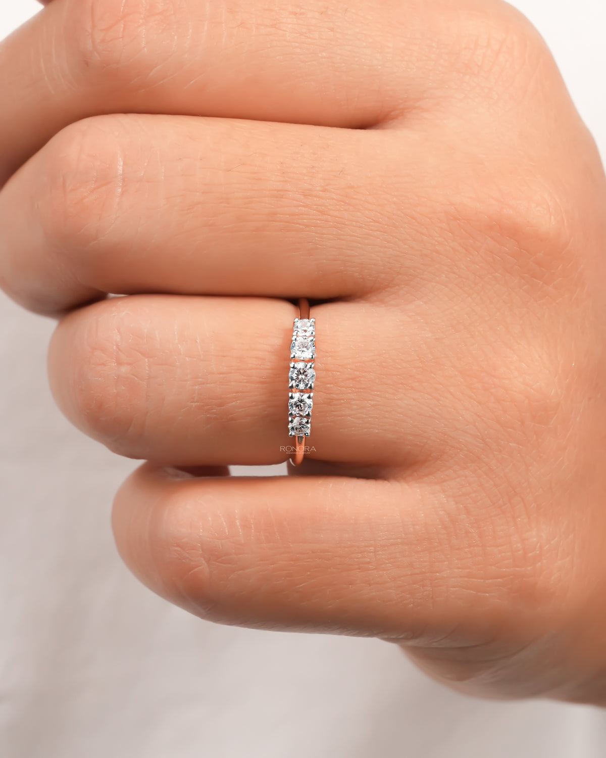 Rose gold five stone lab grown diamond pinky ring worn on a finger, front view of the graduated round stones