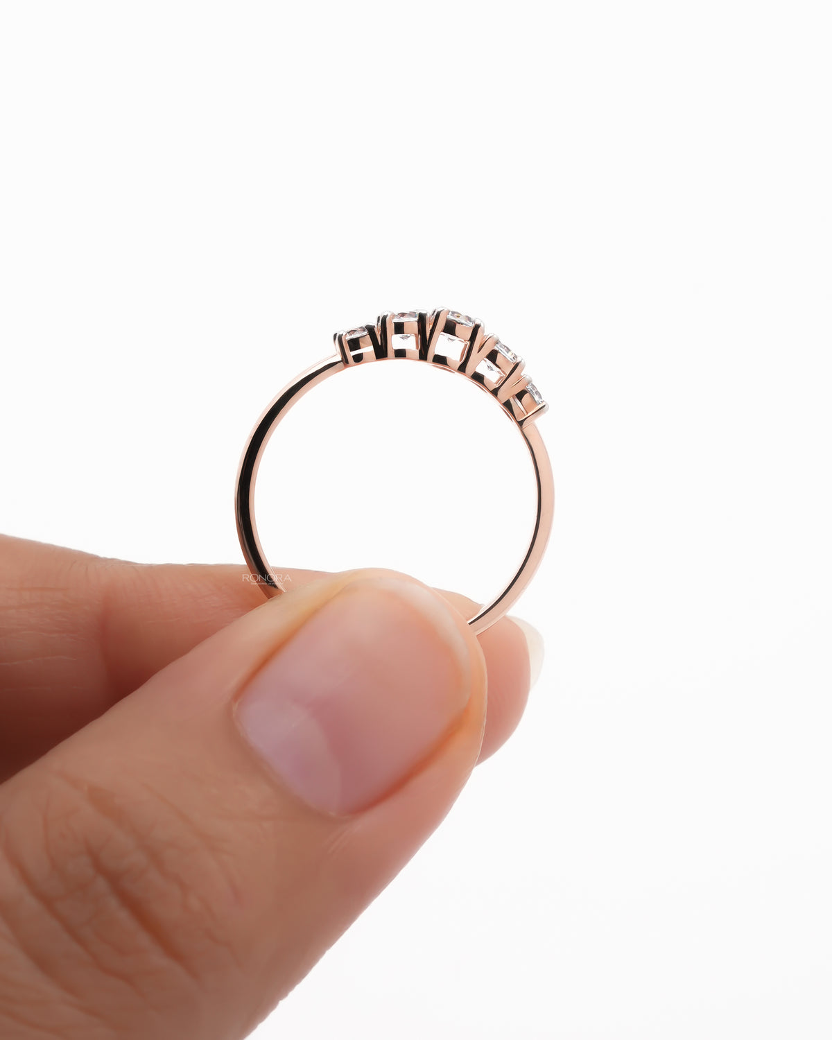 Rose gold five stone lab grown diamond pinky ring held upright between fingers showing the thin dainty band profile