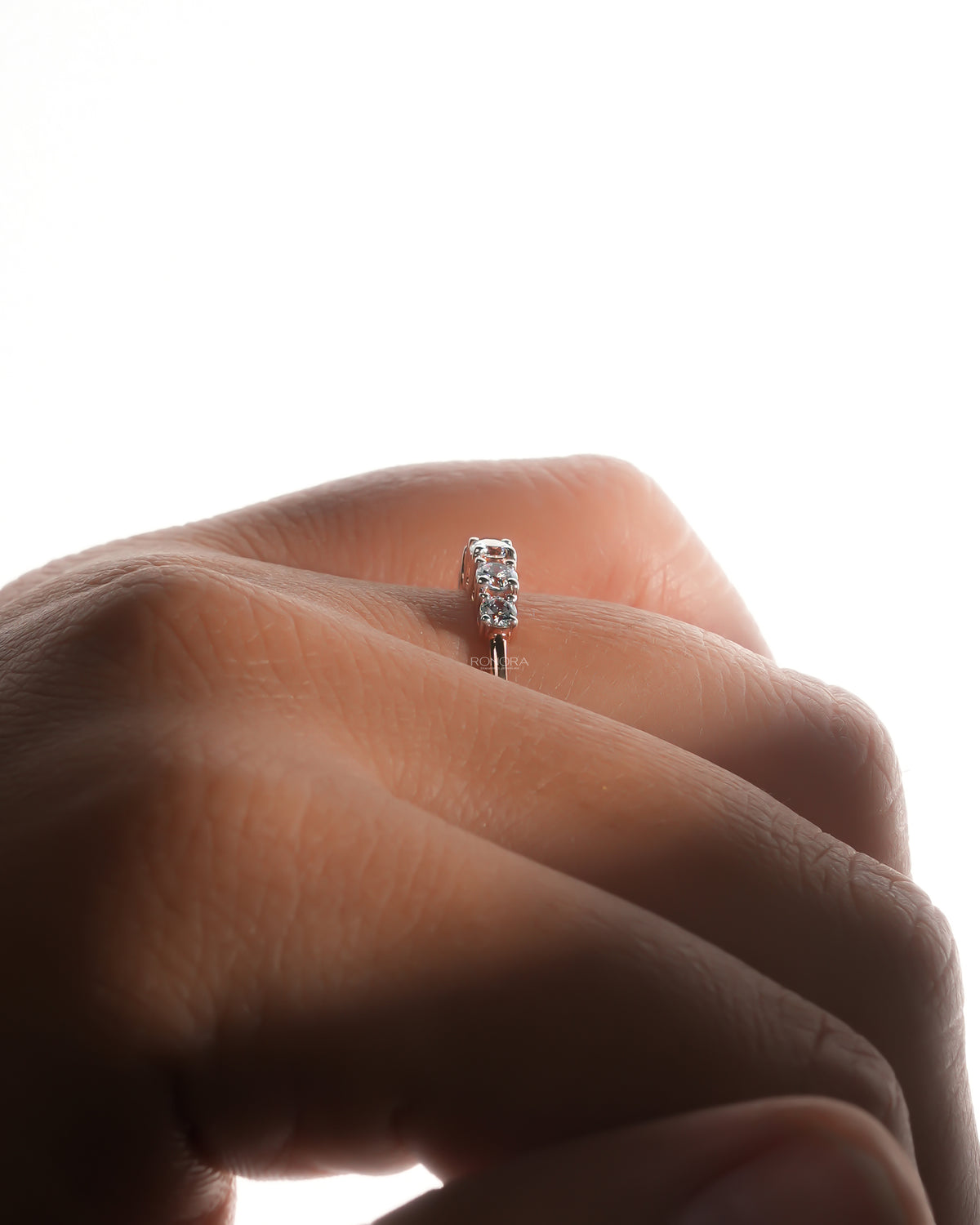 Side view of a five stone lab grown diamond pinky ring on a backlit finger showing the stacked round stones
