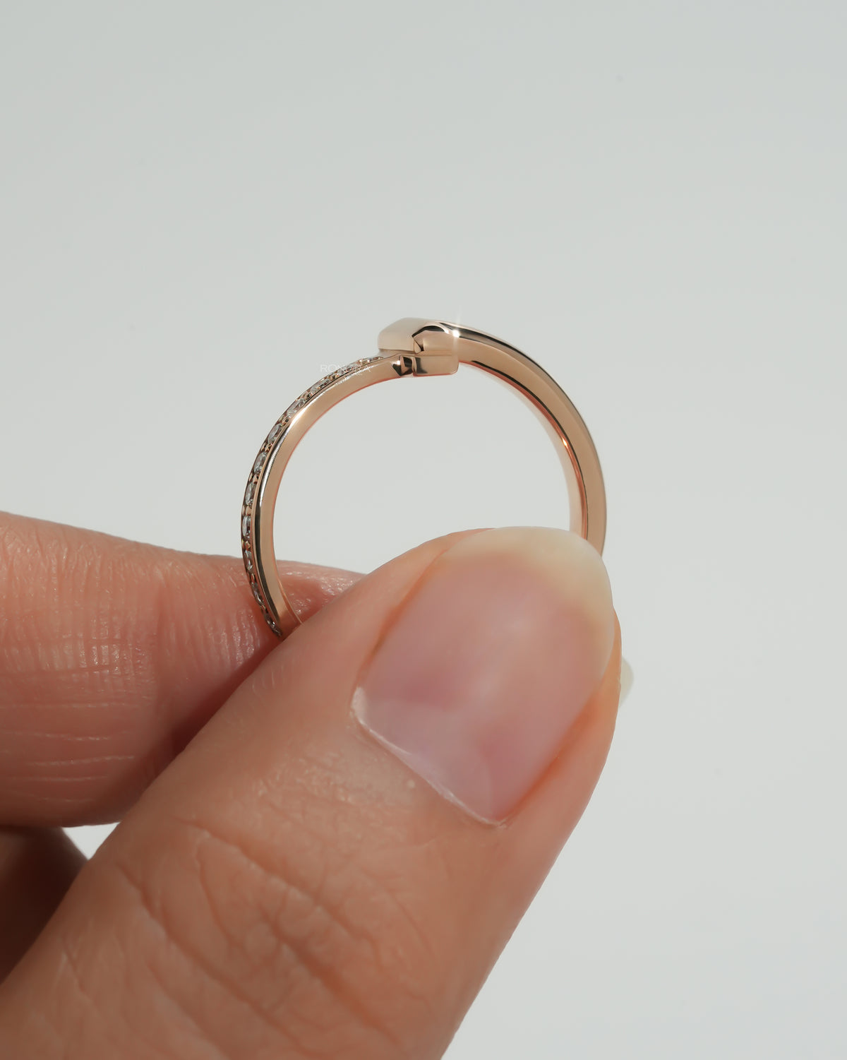 Side profile of a rose gold flat bar lab grown diamond ring with pave diamonds along the band, held between fingers