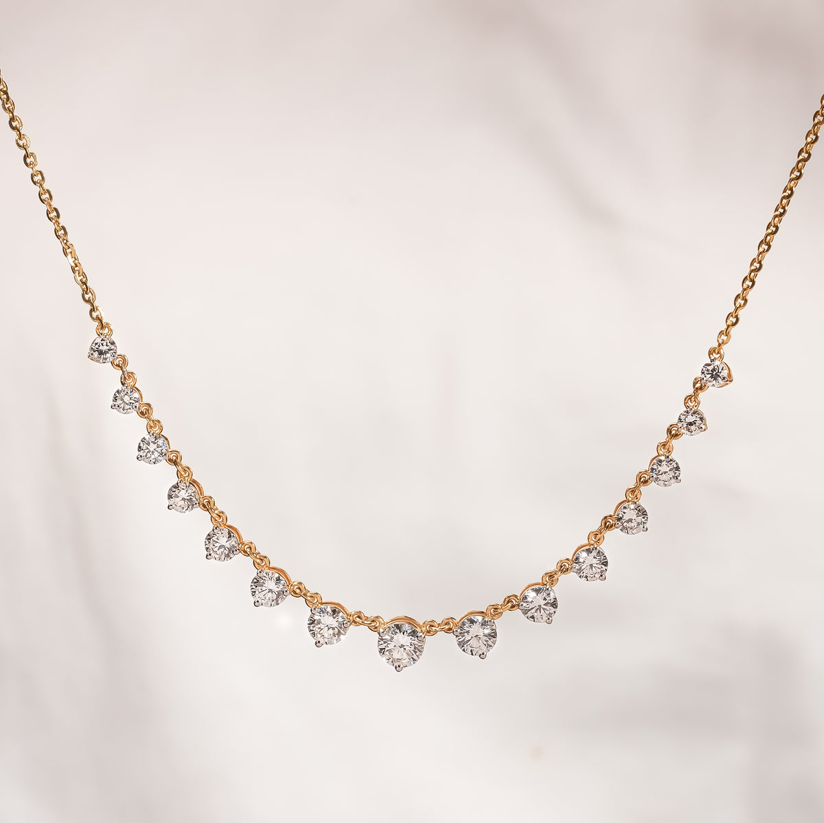 Round lab grown diamond tennis necklace in yellow gold with graduated stones against a soft cream background