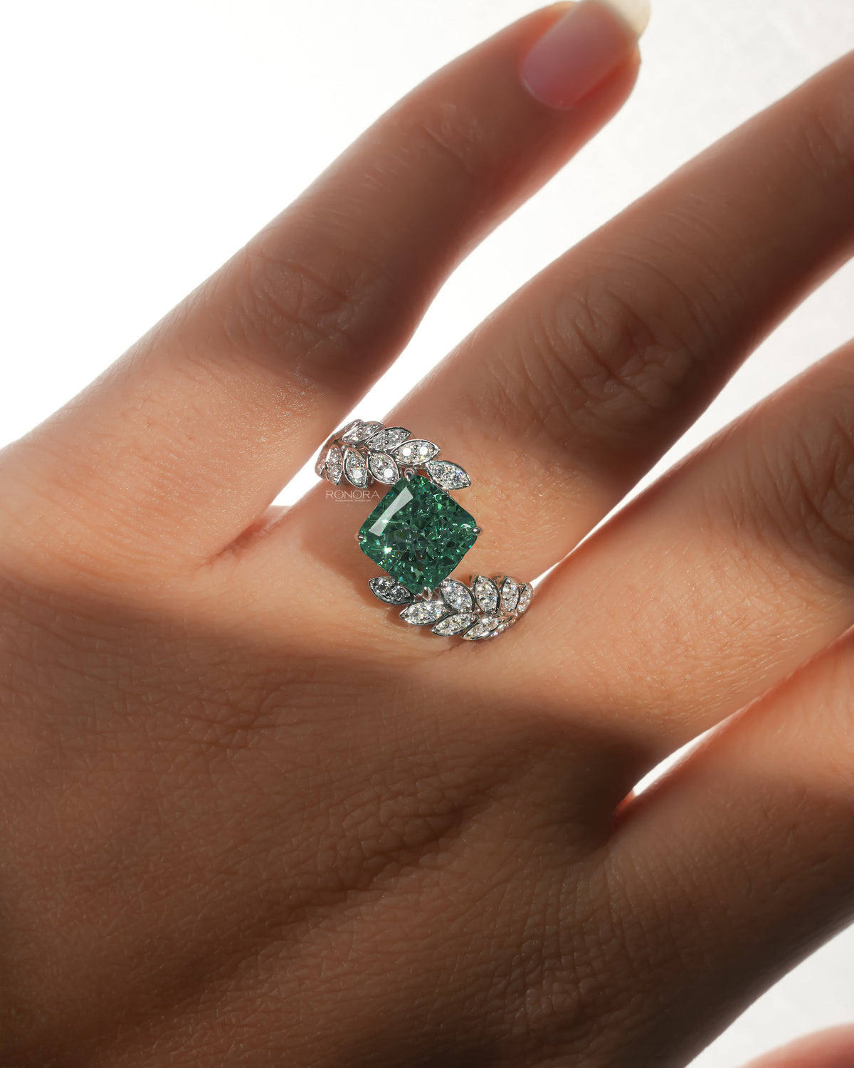 Green cushion lab grown diamond engagement ring in white gold worn on a hand, with leaf sprig diamonds on both sides