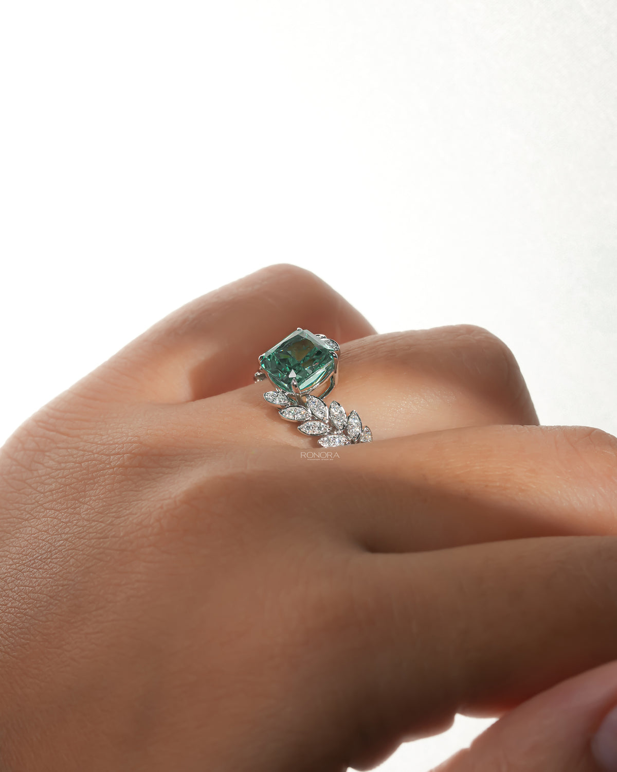 Green cushion lab grown diamond engagement ring on a hand, side angle showing the leaf sprig diamond band