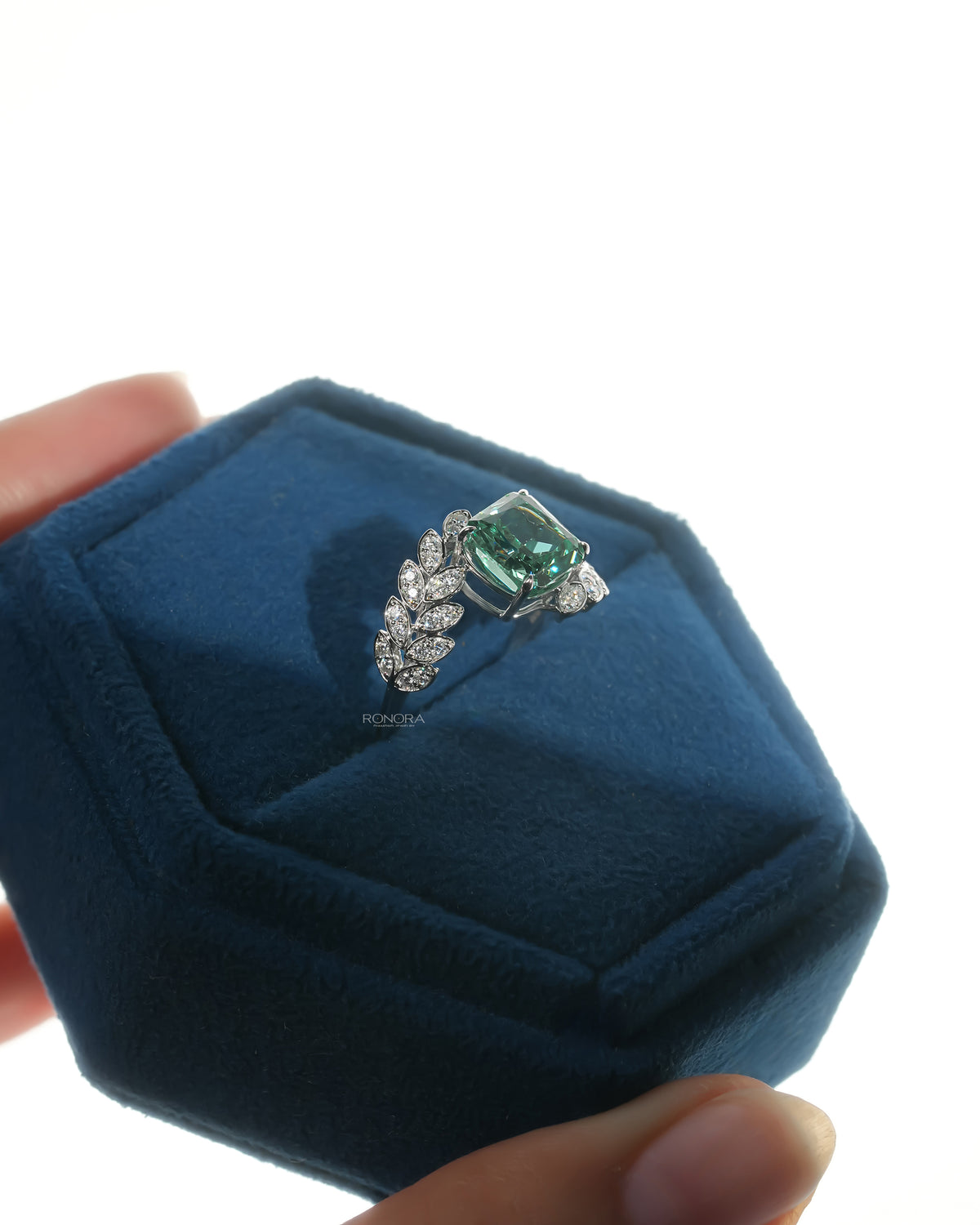 Green cushion lab grown diamond engagement ring in white gold in a blue velvet ring box, angled view