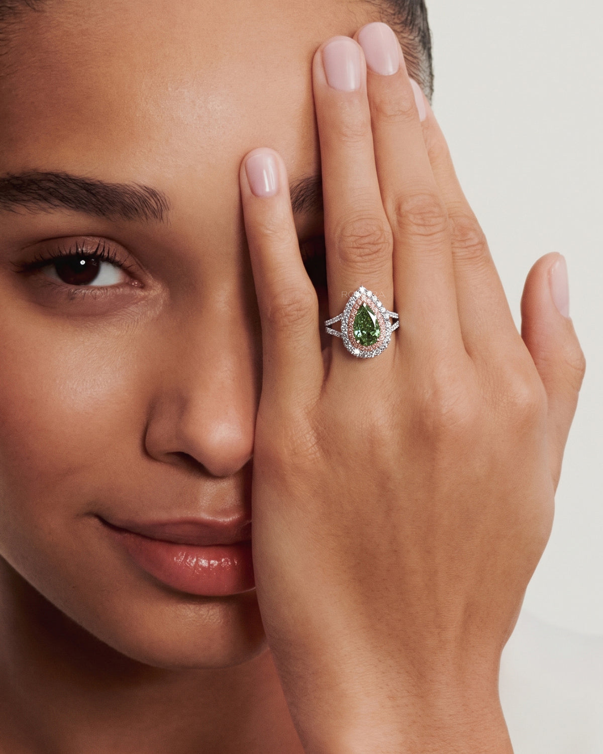 Model wearing a pear green lab grown diamond ring with pink double halo, hand covering one eye