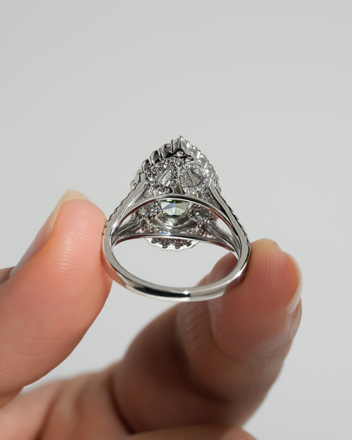 Back view of a pear green lab grown diamond ring with pink double halo and split white gold band held up