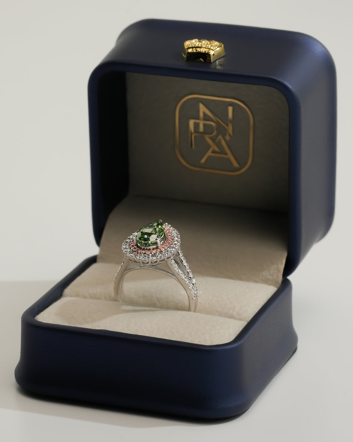 Pear green lab grown diamond ring with pink double halo in an open navy ring box with gold logo