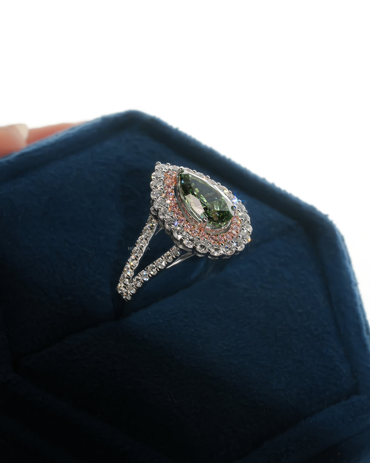 Angled view of a pear green lab grown diamond ring with pink double halo and split band in a velvet box