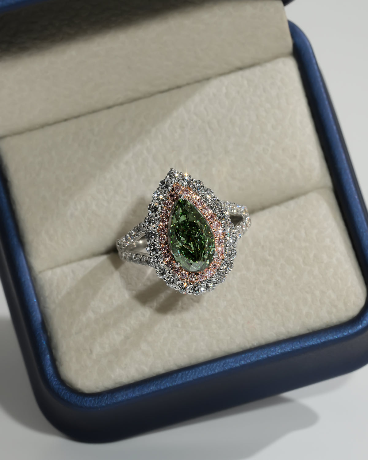 Pear green lab grown diamond ring with pink double halo, top view in a cream ring box with blue edge