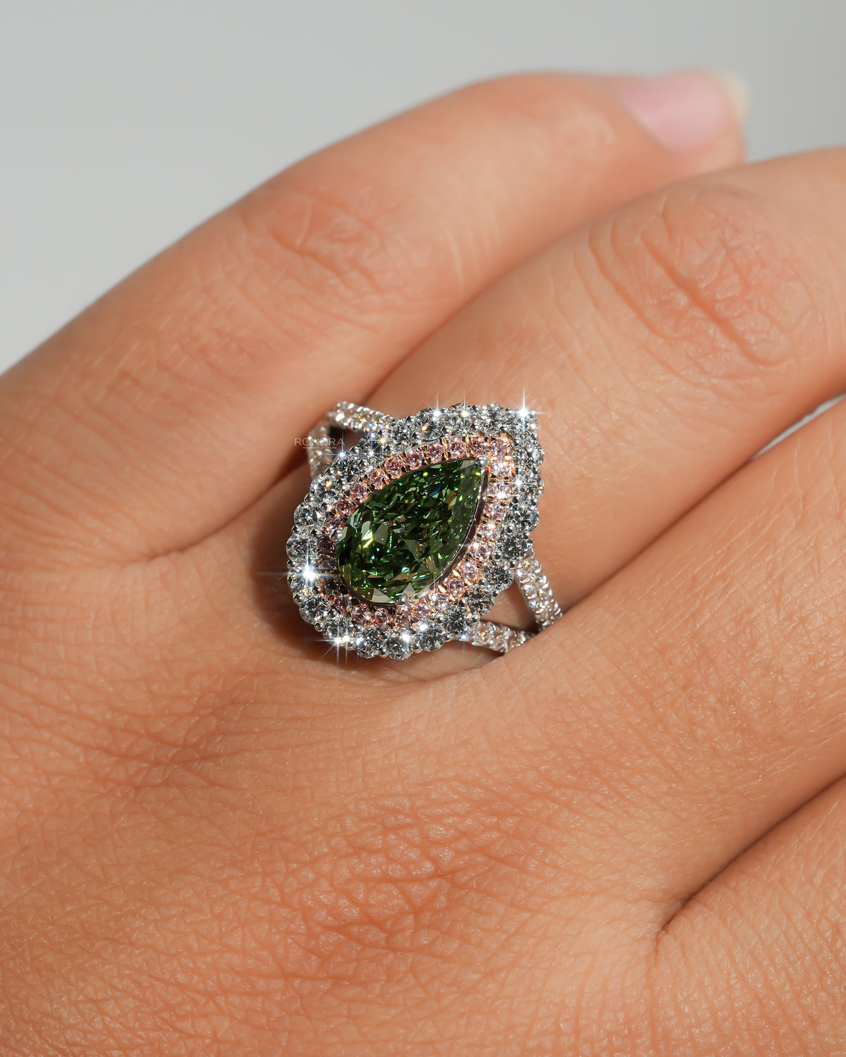 Pear green lab grown diamond ring with pink double halo worn on a hand, close-up with sparkling halo