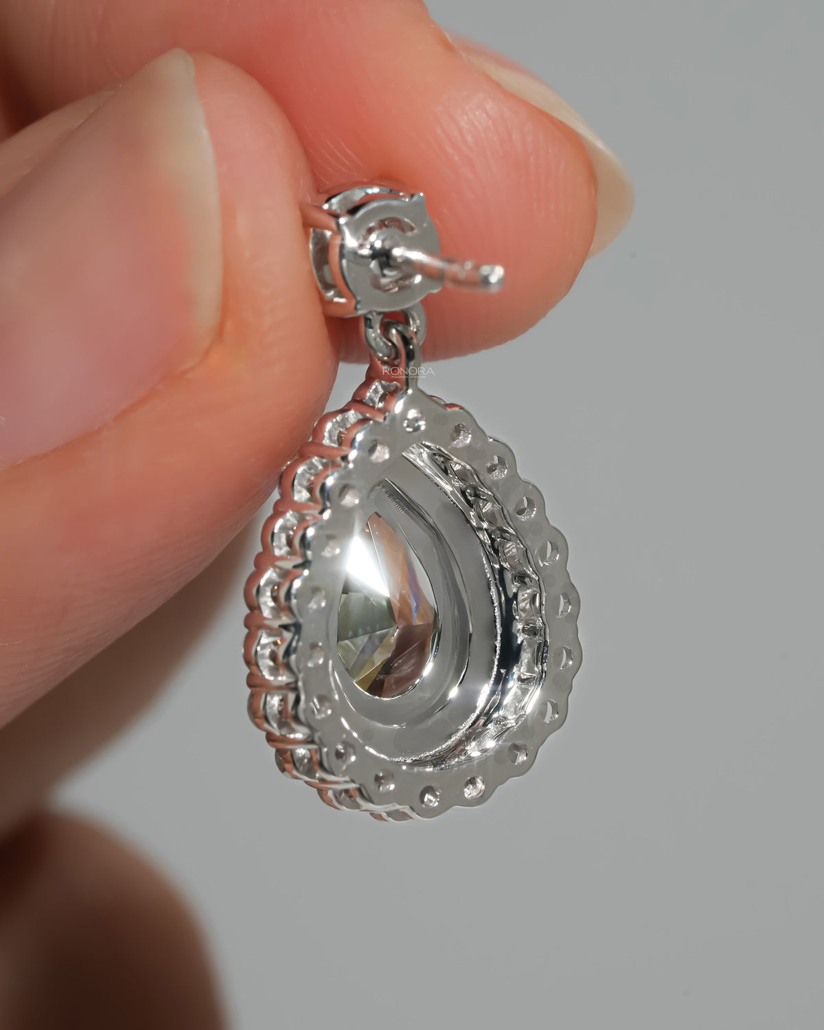 Back of green pear lab grown diamond drop earrings in white gold held between fingers, showing the post and halo