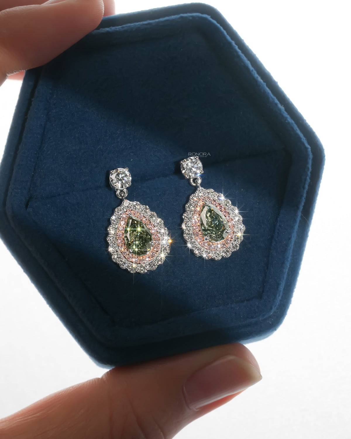 Pair of green pear lab grown diamond drop earrings with pink double halo in a blue velvet hexagon jewelry box
