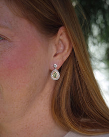 Woman wearing green pear lab grown diamond drop earrings with a pink and white diamond double halo in white gold