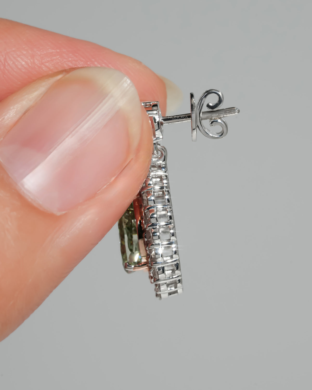 Side view of green pear lab grown diamond drop earrings held in fingers, showing the white gold post and halo depth