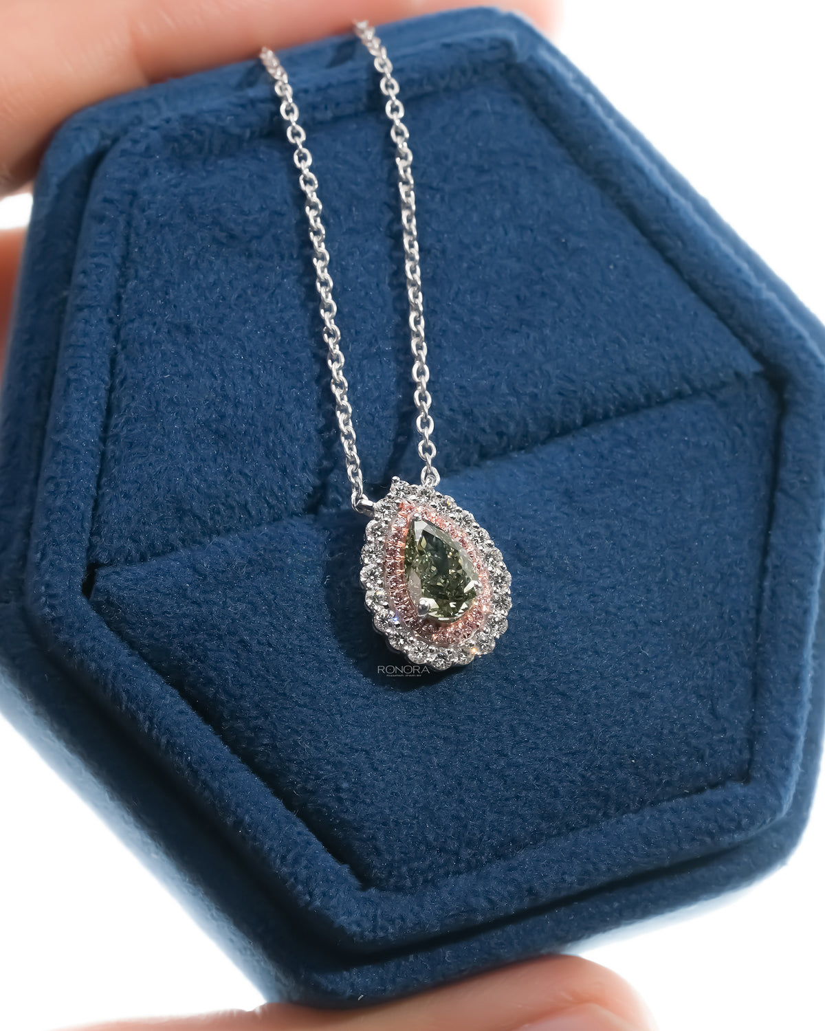 Green pear lab grown diamond pendant with a pink double halo in a blue velvet ring box held in hand