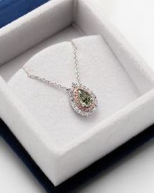 Green pear lab grown diamond pendant with a pink double halo resting in a white velvet jewelry box