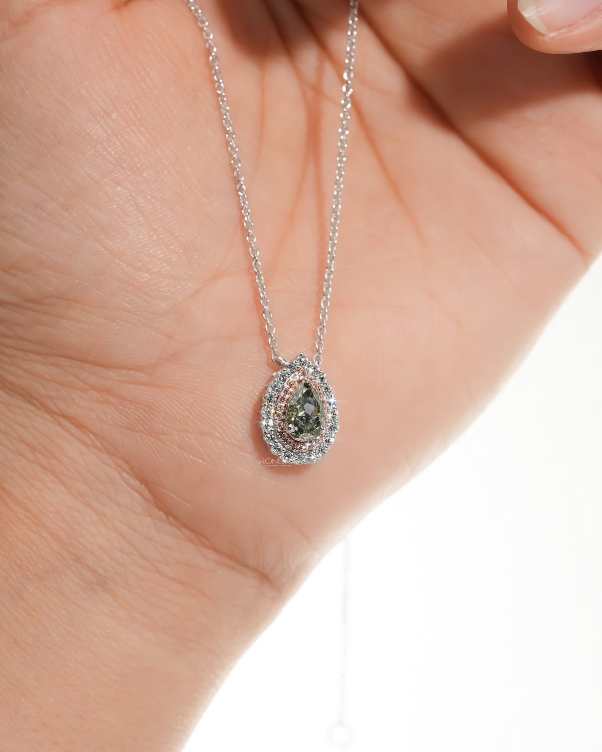 Close view of a green pear lab grown diamond pendant, pink double halo, resting on an open palm on a white gold chain