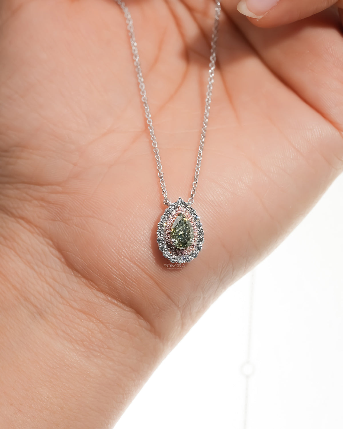 Green pear lab grown diamond pendant with a pink and white double halo hanging over an open palm