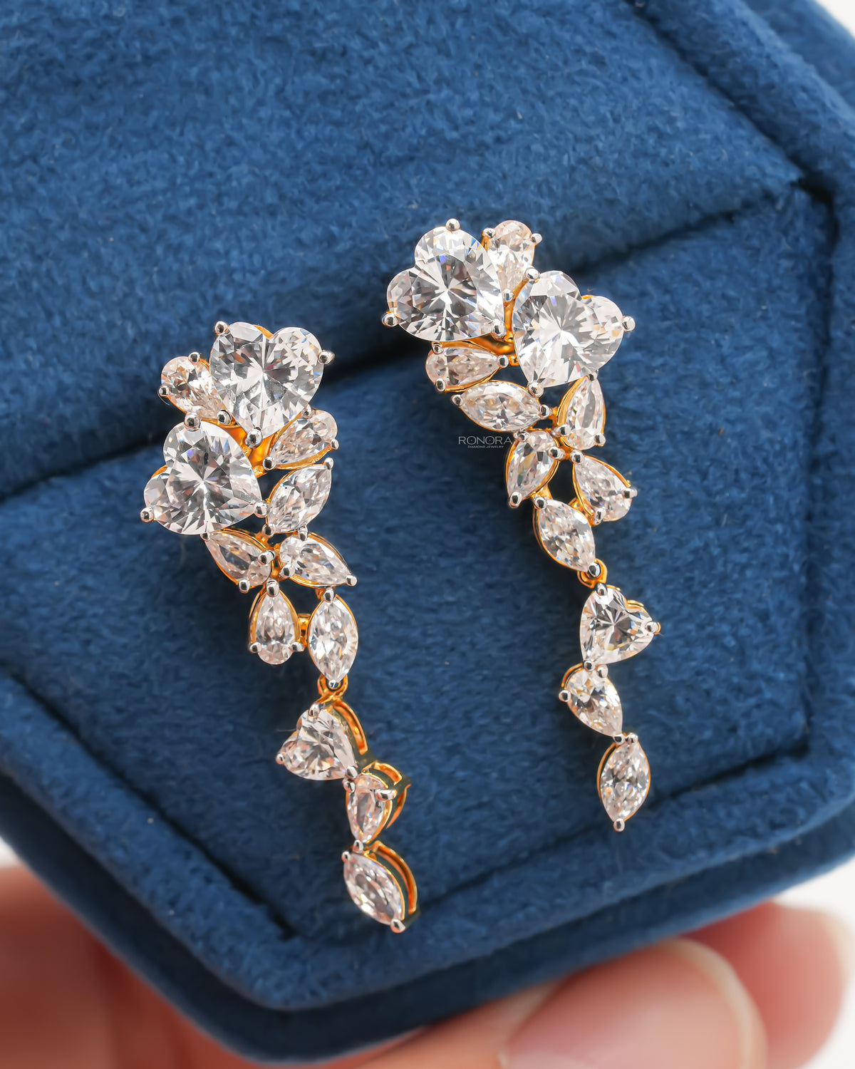 Close-up of heart lab grown diamond drop earrings in yellow gold with pear and marquise stones on blue velvet