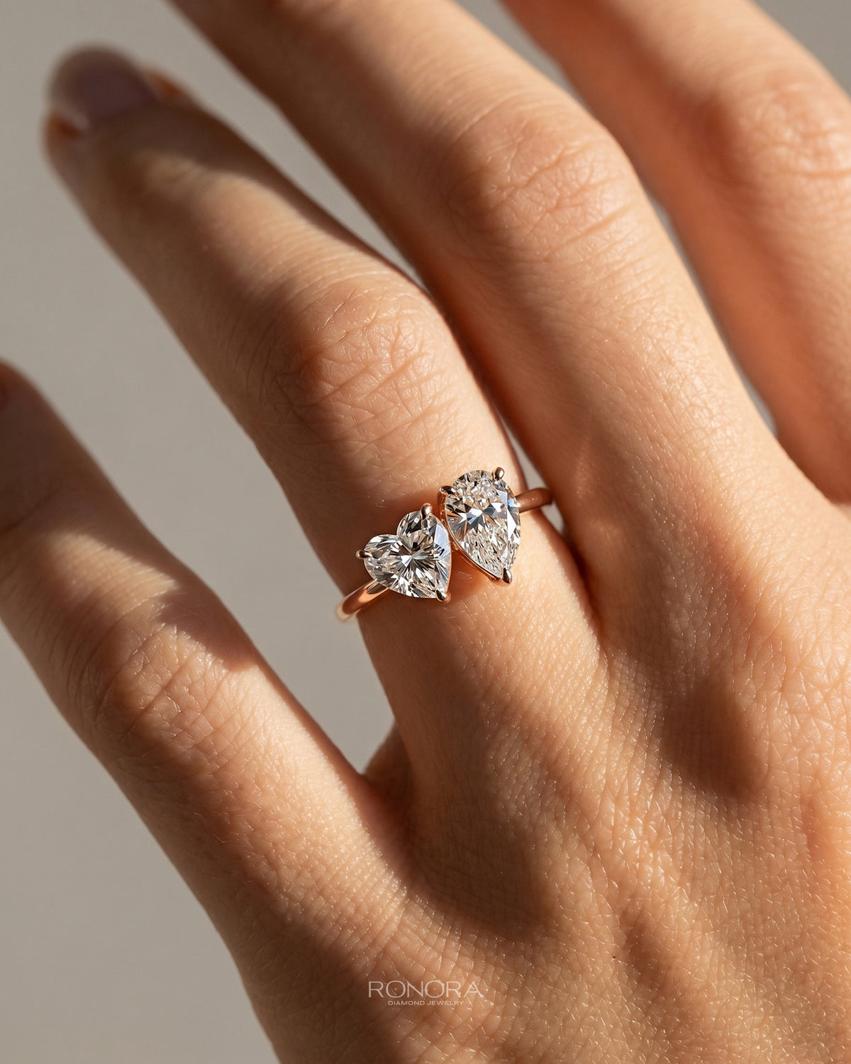 Hand wearing a heart and pear moissanite toi et moi ring in rose gold, two stones set side by side