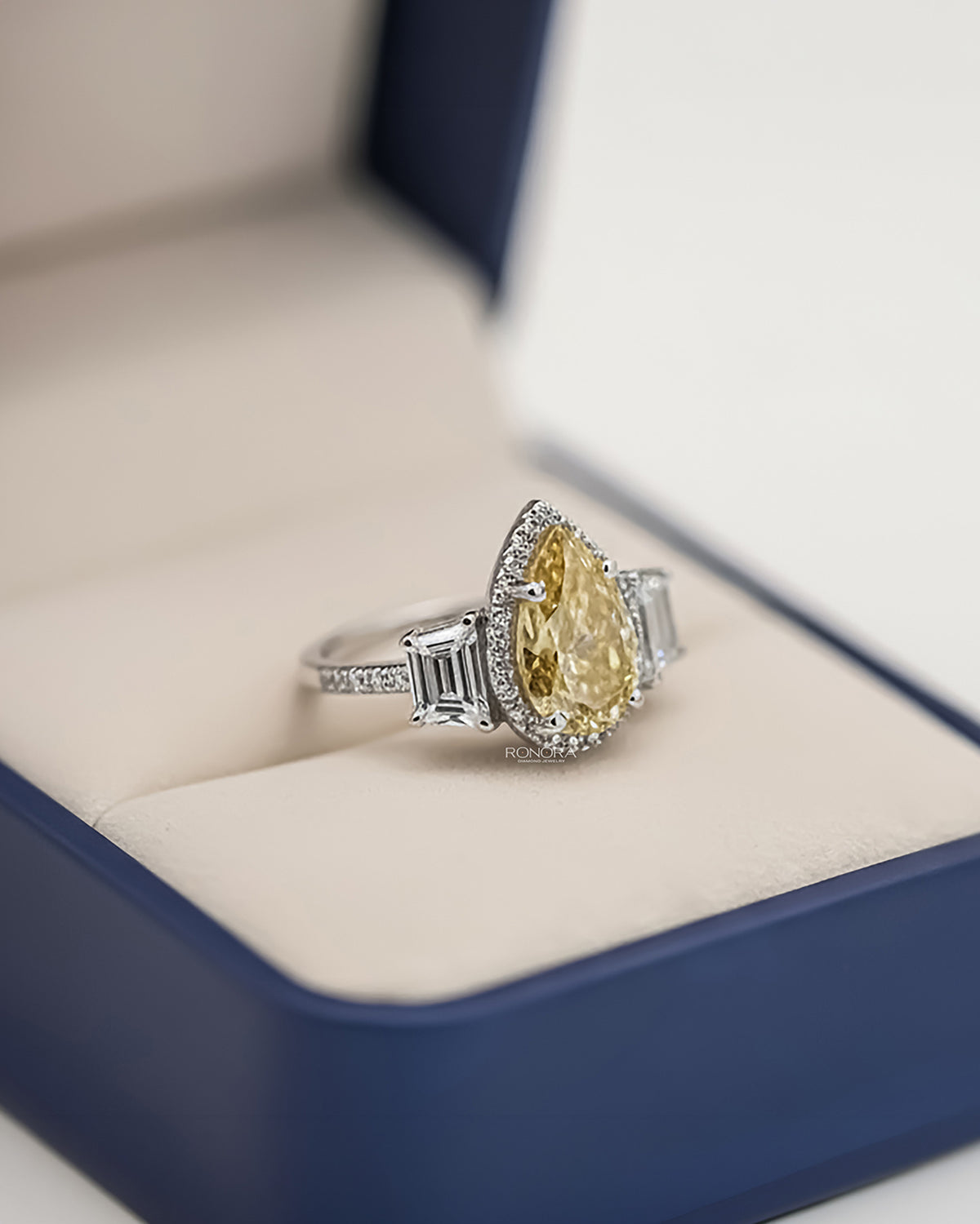 Angled view of yellow pear lab grown diamond halo ring with halo three-stone setting