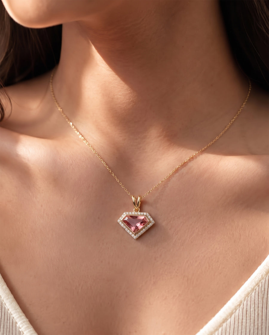 Woman wearing a pink shield cut lab grown diamond necklace with a halo on a fine yellow gold chain, close-up