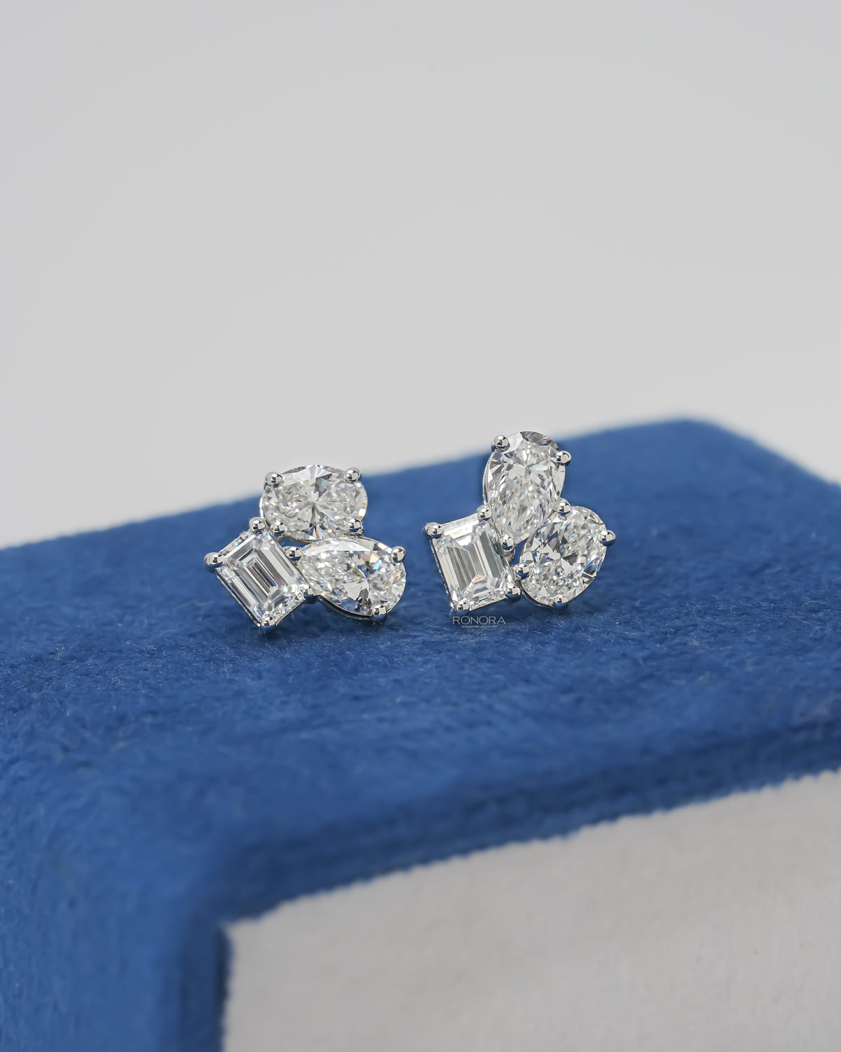 Lab grown diamond cluster stud earrings with emerald, pear and oval cut stones in white gold on blue velvet