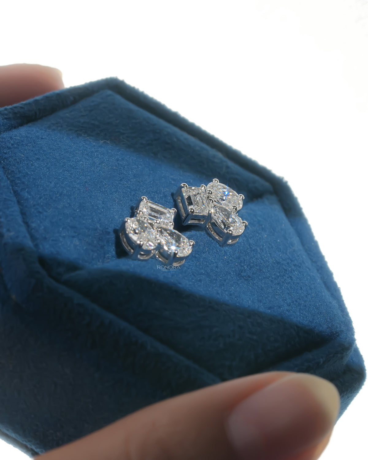 Angled view of lab grown diamond cluster stud earrings with mixed shape stones in a blue velvet jewelry box