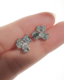 Pair of lab grown diamond cluster stud earrings on a fingertip, showing emerald, pear and oval cut stones