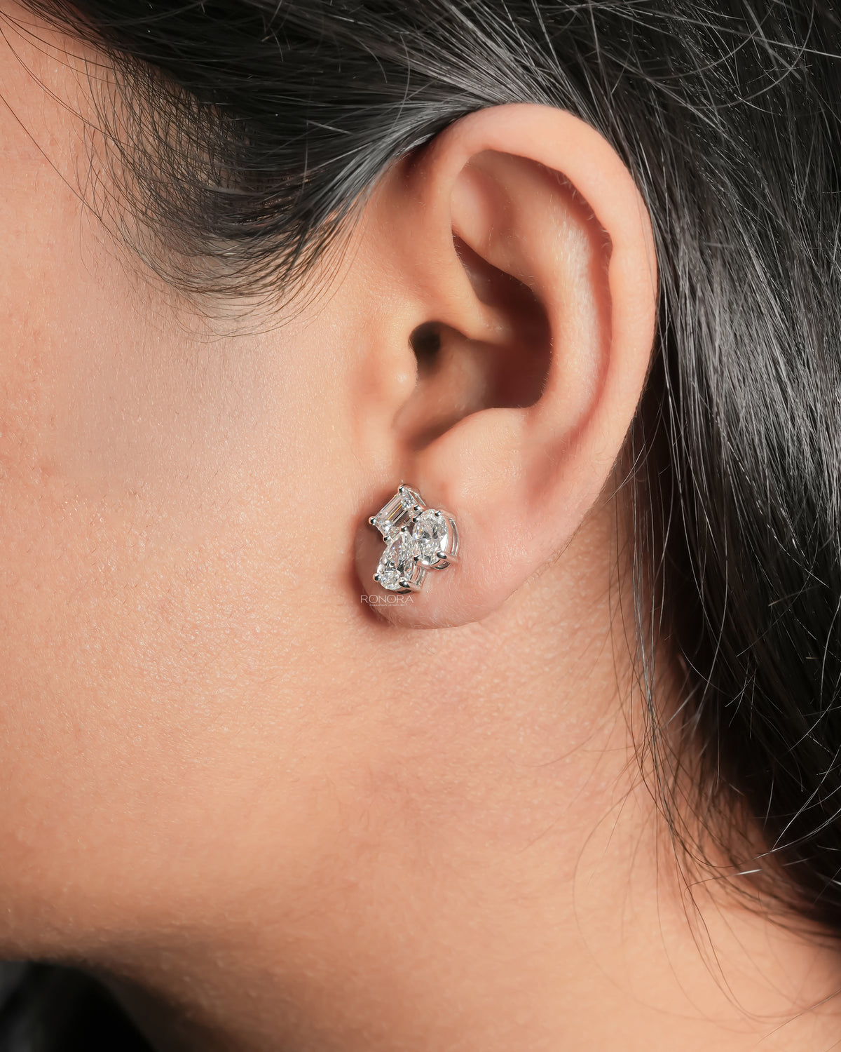 Ear wearing a lab grown diamond cluster stud earring with emerald, pear and oval cut diamonds in white gold